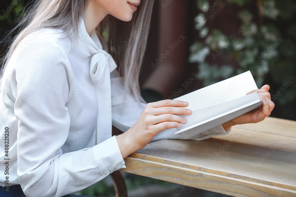 Beautiful woman reading blank book in cafe outdoors