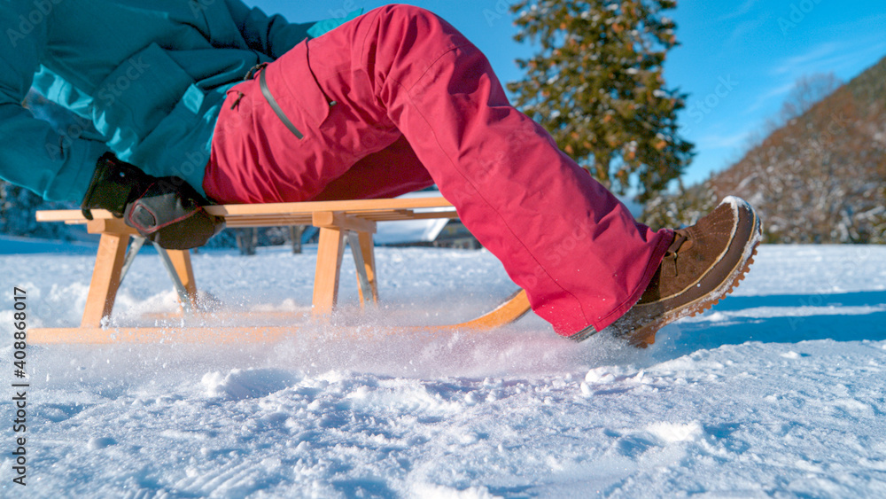 LOW ANGLE, CLOSE UP: Unrecognizable young woman sleds across the snowy meadow.