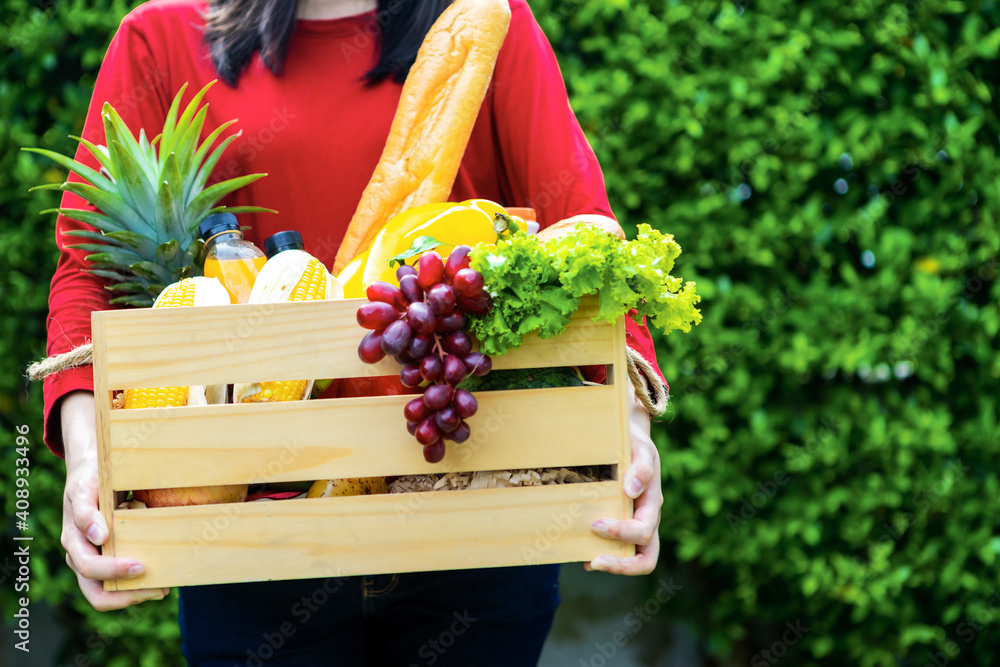 亚洲女人拿着装有蔬菜的木制篮子。篮子里的新鲜蔬菜。花园里的野餐