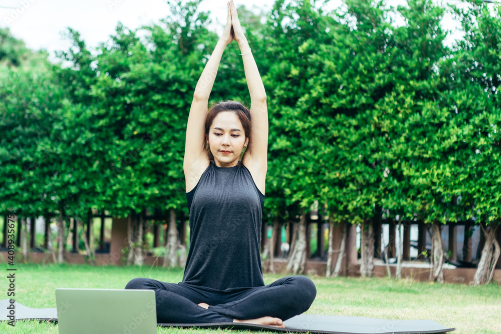 放松健康运动穿着健身服的亚洲女性在公园冥想，使用在线流媒体瑜伽