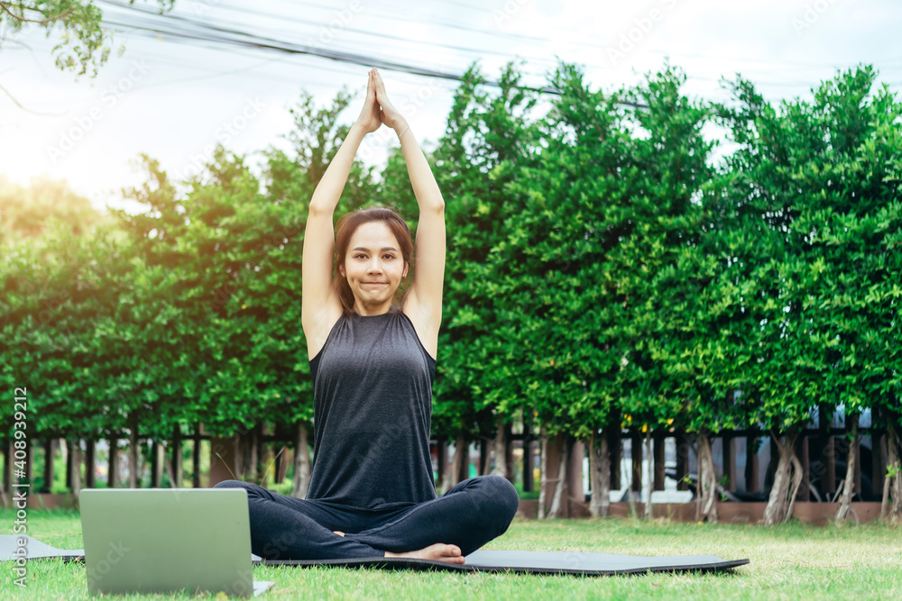 Relaxed healthy sports Asian woman in fitness clothes at park meditating using online streaming yoga