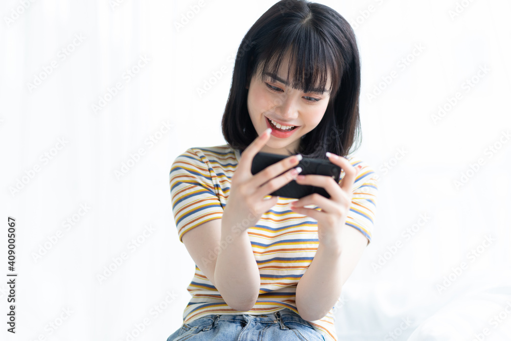 漂亮的亚洲女人在卧室用智能手机玩游戏