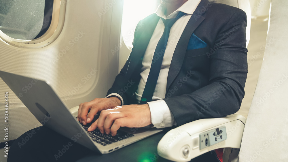 年轻商人在飞机上使用笔记本电脑。商务旅行概念。