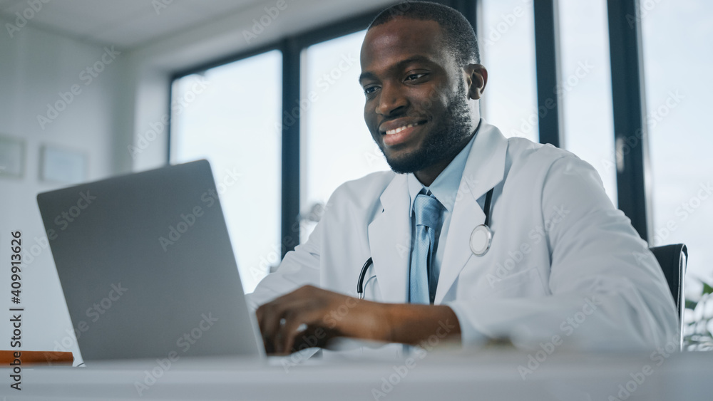快乐的非裔美国家庭医生正在健康诊所的笔记本电脑上工作。物理