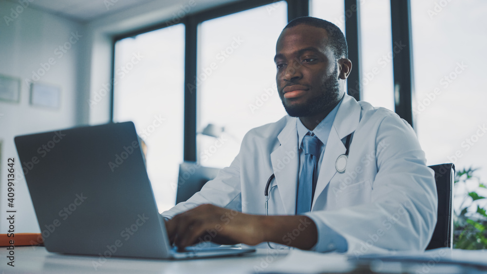 严重的非裔美国家庭医生正在健康诊所使用笔记本电脑。P