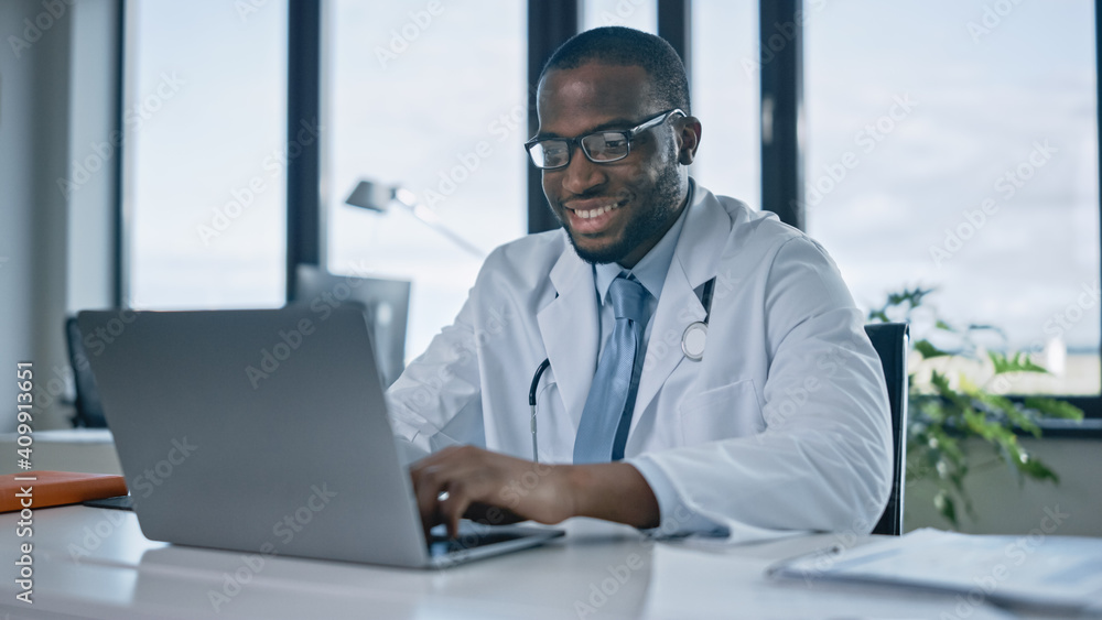 快乐的非裔美国家庭医生正在健康诊所的笔记本电脑上工作。物理