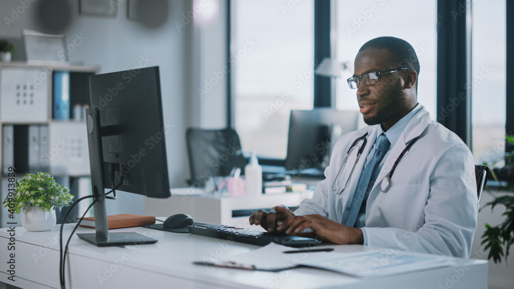 冷静的非裔美国家庭医生戴着眼镜在健康中的台式电脑上工作