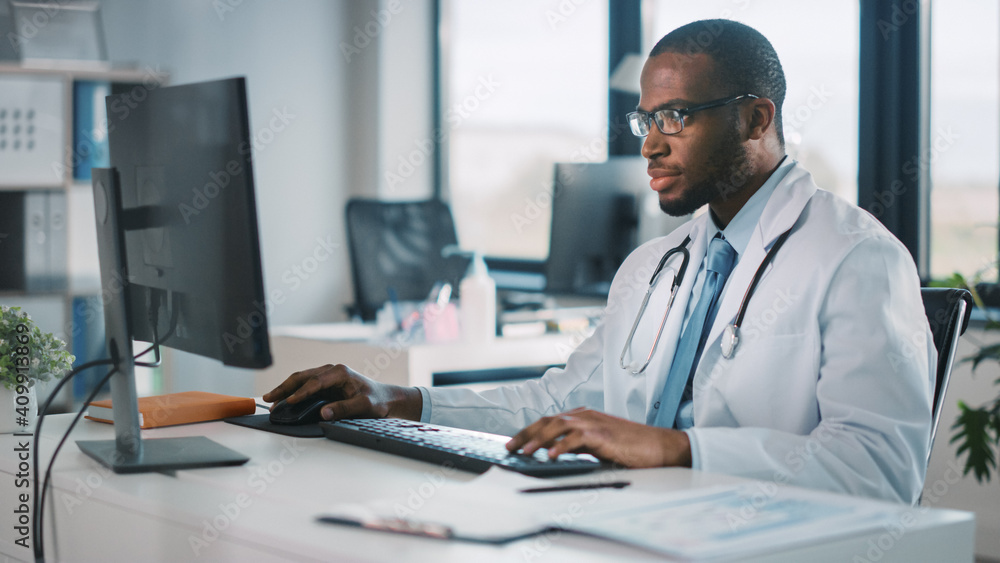 冷静的非裔美国家庭医生戴着眼镜在健康中的台式电脑上工作