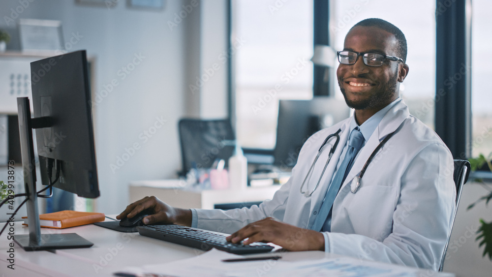 戴眼镜的非裔美国家庭医生在诊所的电脑上工作。成功