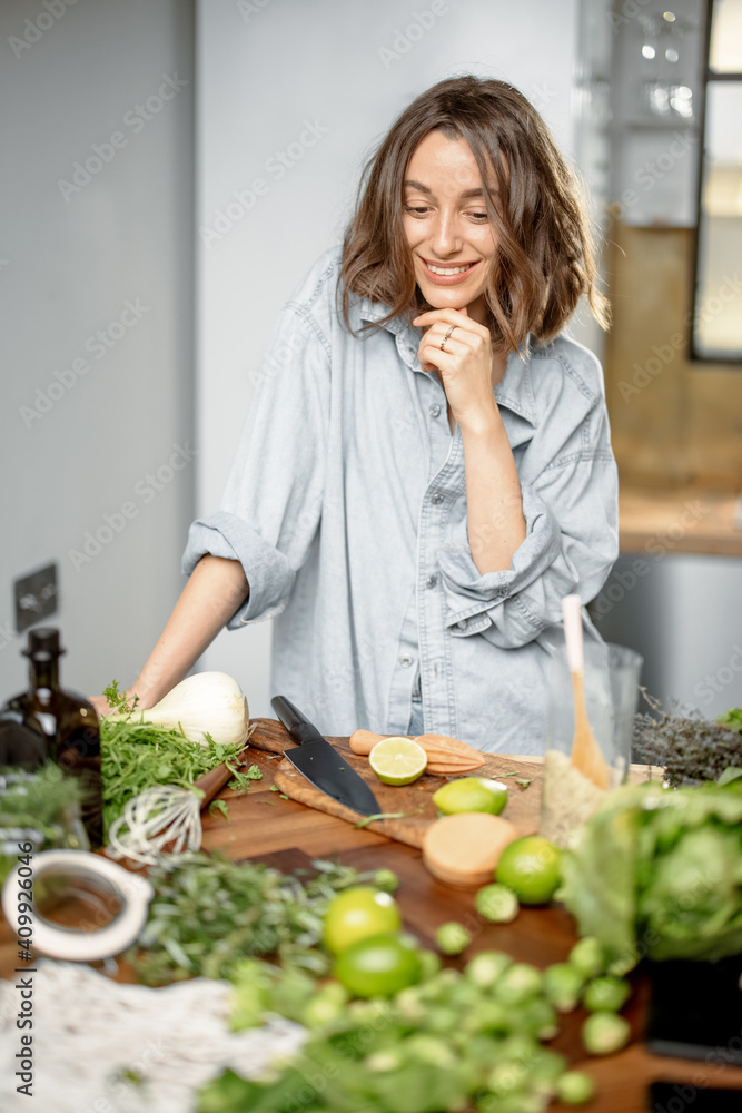 带着绿色食材的漂亮女人正在考虑在厨房里烹饪健康的食物。健康和