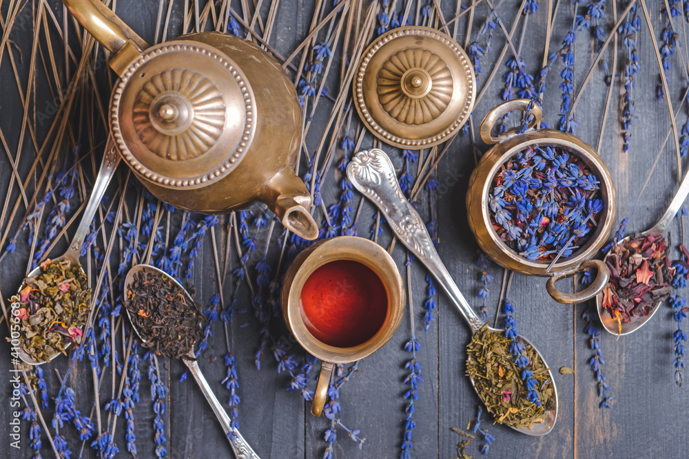 Teapot and spoons with different dry tea leaves on wooden background