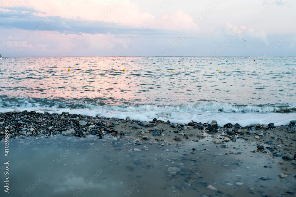 雨后，海滩上有一片美丽的多云日落，前滨布满鹅卵石，还有一个水坑。