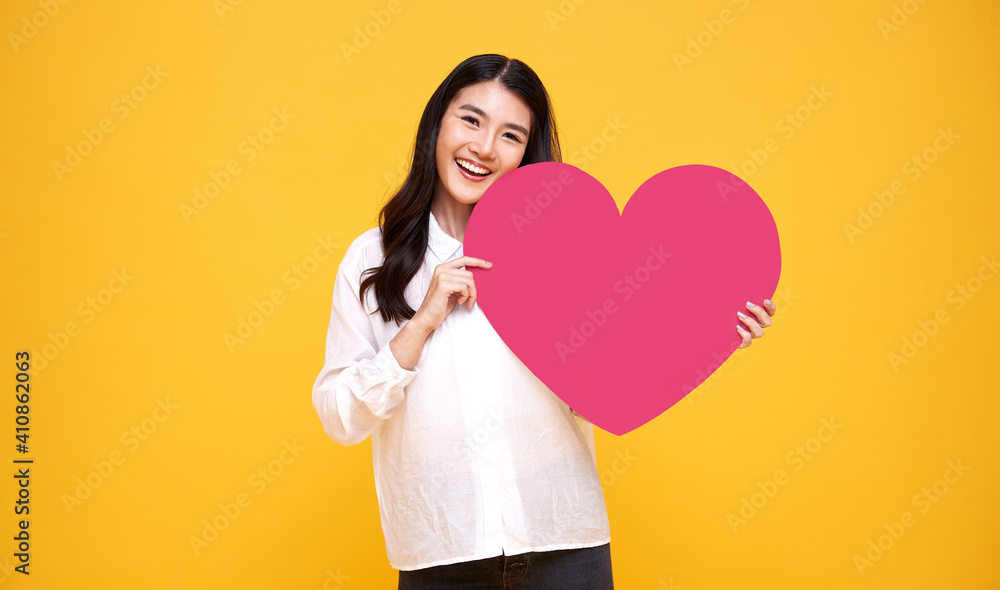 年轻美丽的亚洲女性在黄色背景下显示出红色的心形标志。爱和幸福的val