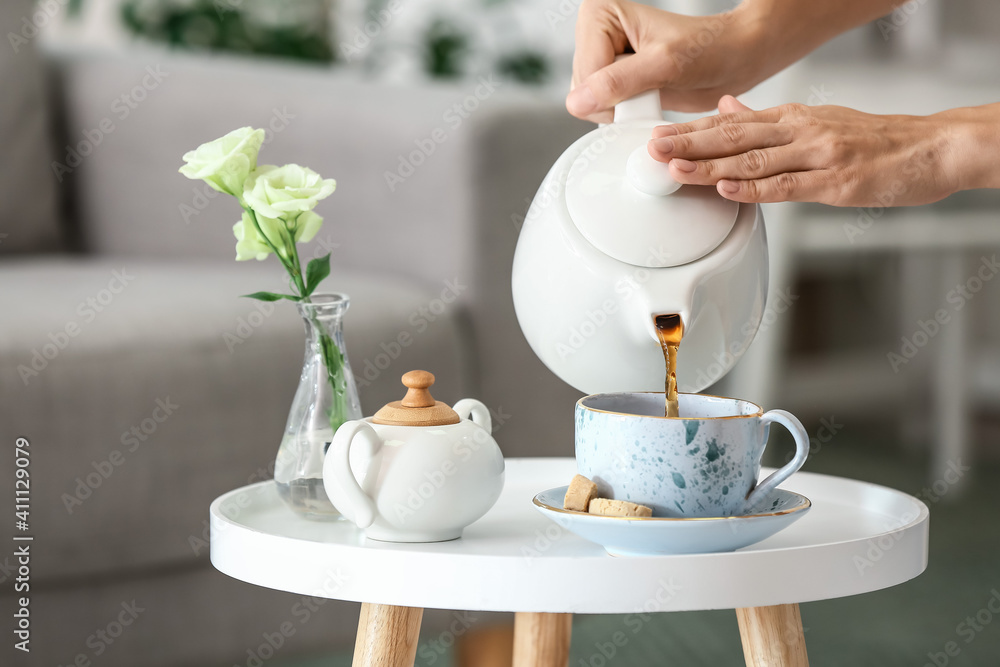 女人把茶壶里的热茶倒进桌子上的杯子里