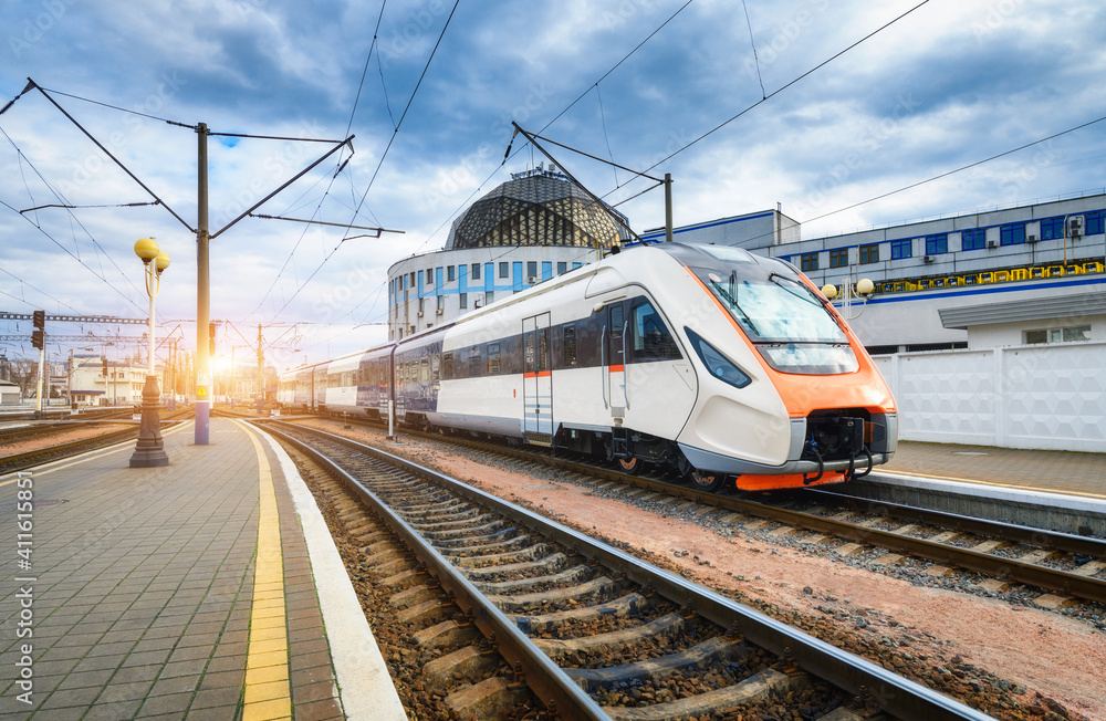 High speed train on the railway station at sunset. Industrial landscape with moving modern intercity