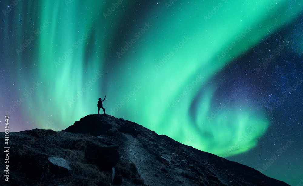 Northern lights and silhouette of standing man with raised up arms on the mountain in Norway. Aurora