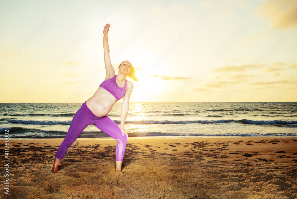 孕妇在沙滩上锻炼伸展运动，背景是海洋上的日落
