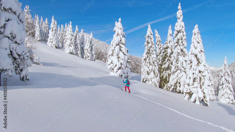 空中飞航：在一个阳光明媚的日子里，一名身材健美的年轻女子在雪地上徒步旅行。