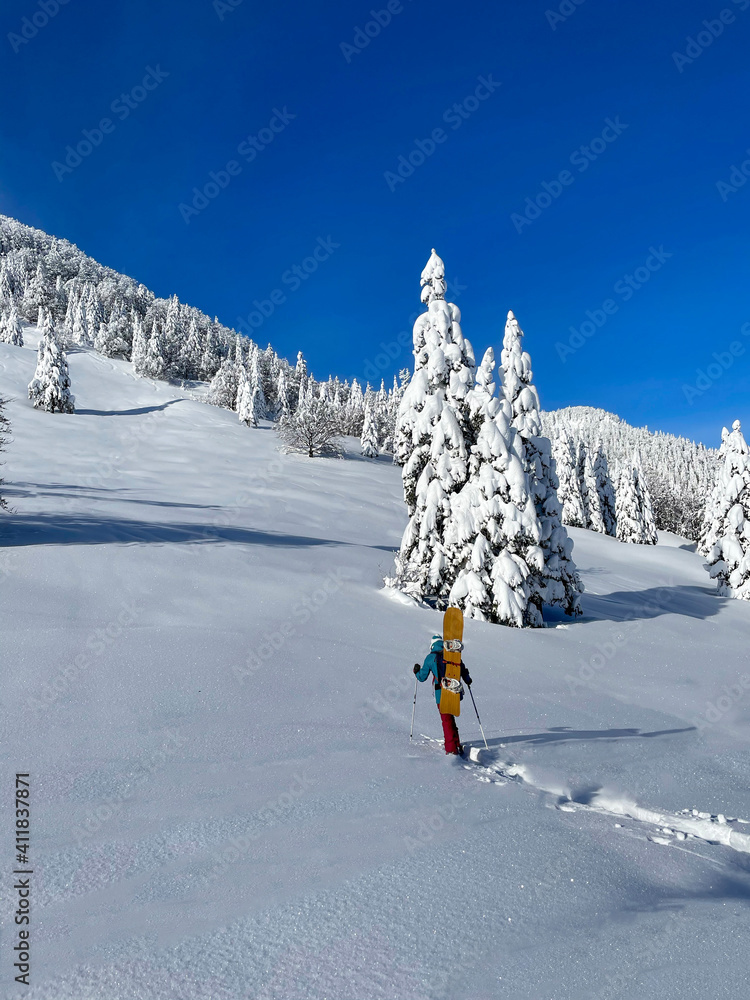 垂直：运动型女子单板滑雪板运动员穿着雪鞋登上雪山，在雪地上骑行。
