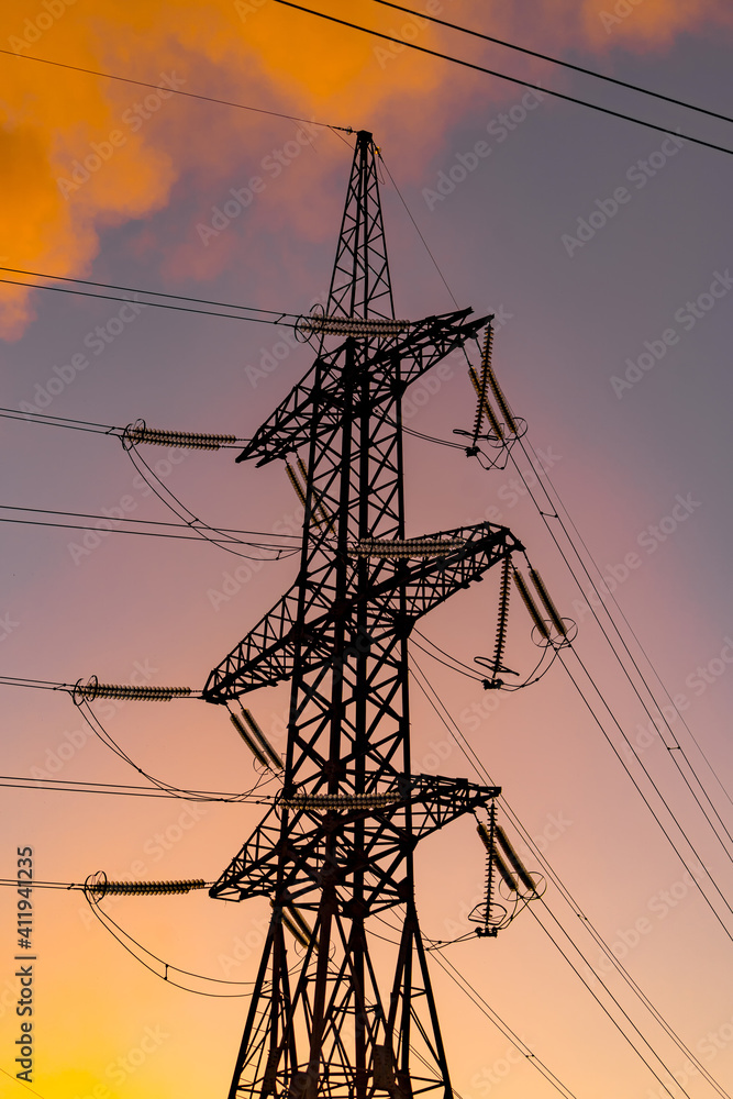 Metal electric pillar with orange sky background. Power transmission facilities. High voltage pylons