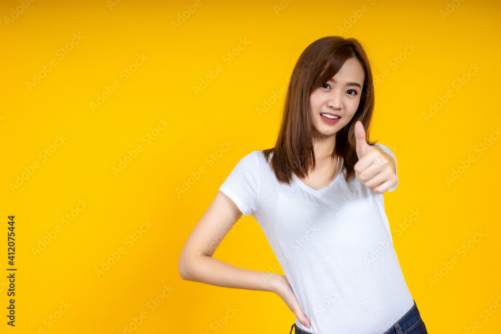 年轻优雅的亚洲女性微笑着展示拇指向上的黄色背景隔离复制空间