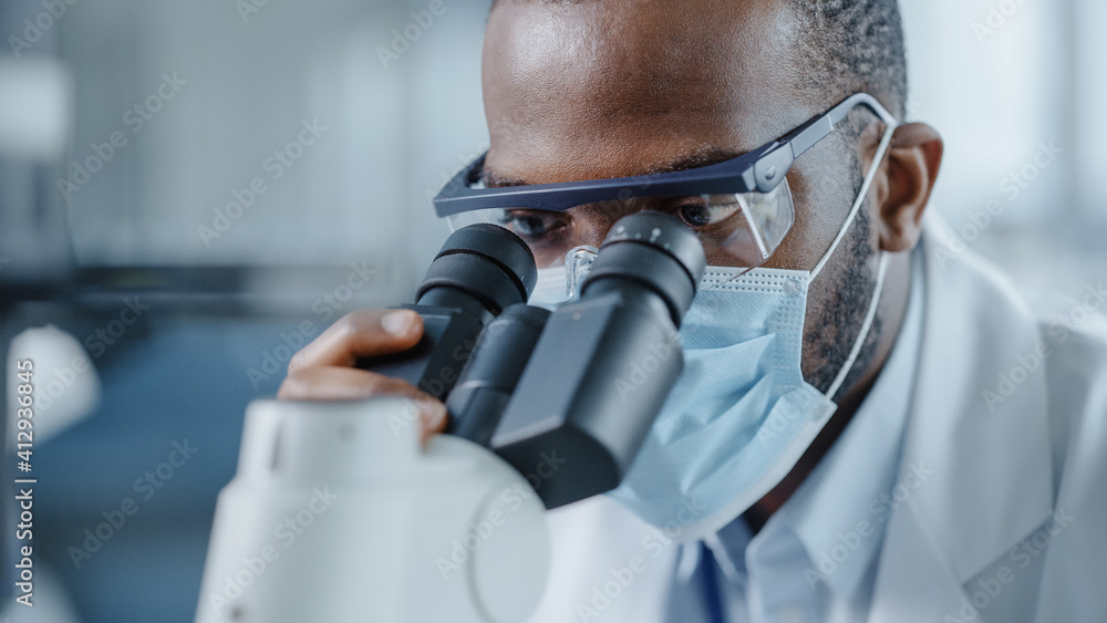 一位英俊的黑人男科学家戴着口罩看着显微镜的特写镜头。