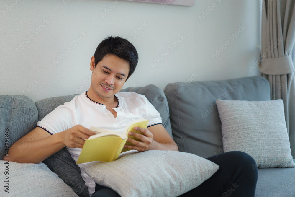 亚洲男子坐在家里客厅的沙发上看书。