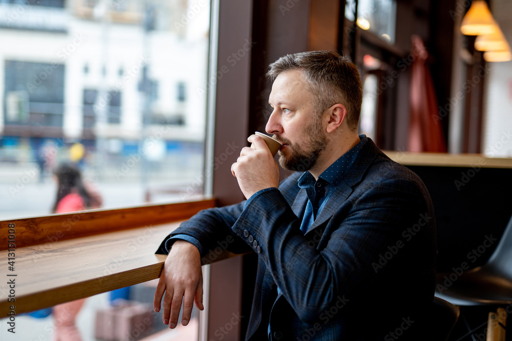 一个穿着夹克和牛仔裤的男人正在餐厅休息，喝着一杯咖啡。一个年轻商人的画像