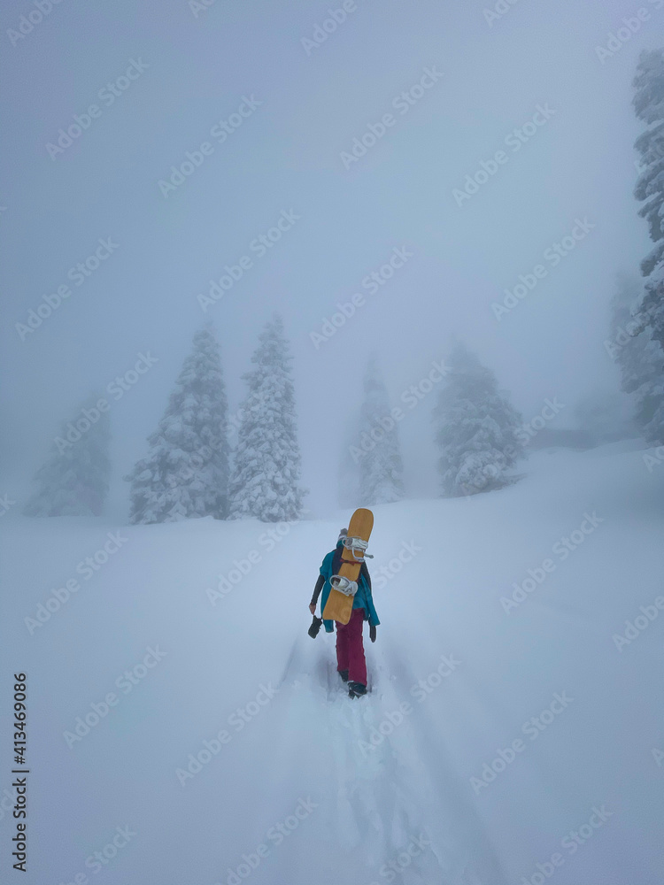 垂直：年轻的女性单板滑雪运动员爬上一座覆盖着新鲜粉末雪的小山。