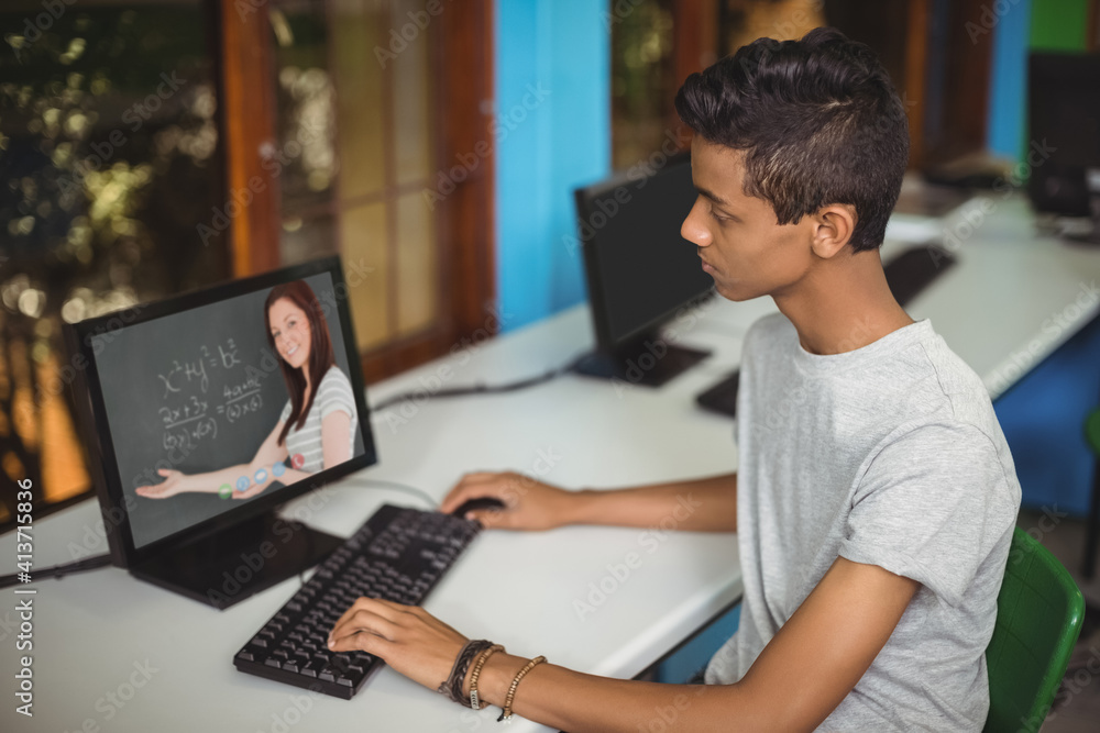 Male indian student having a video call with female teacher on computer at school