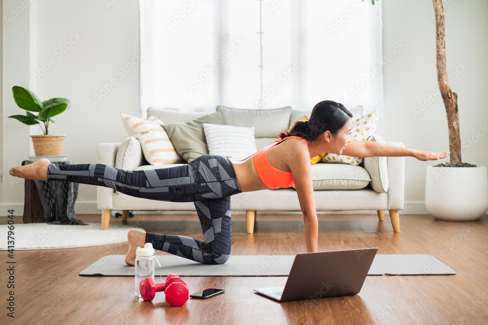 运动型女性在家做瑜伽和锻炼，在笔记本电脑上与教练在线锻炼