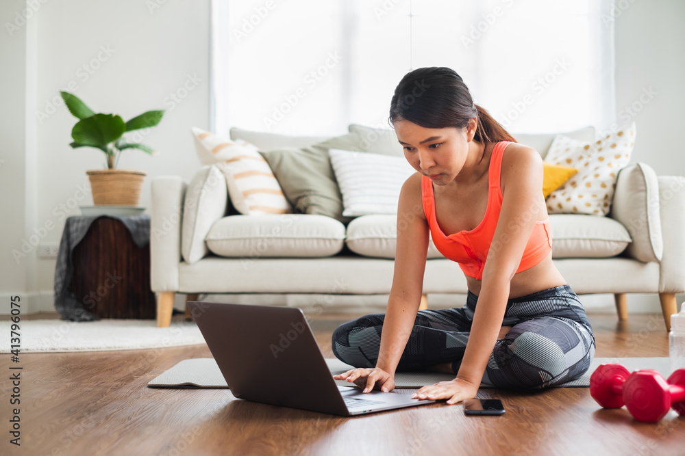 运动型女性观看和学习锻炼，在笔记本电脑屏幕上与教练在线瑜伽