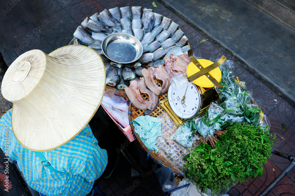戴着斗笠的街头小贩，在泰国街头卖干鱼