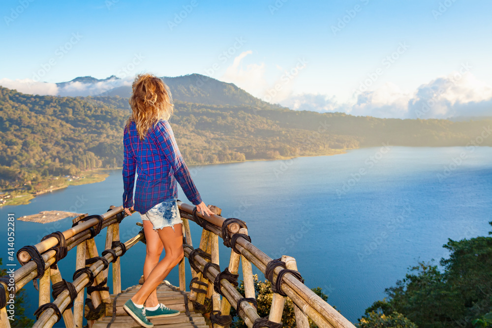 夏日家庭度假。年轻女子站在高高的悬崖上的阳台上。快乐的女孩看着令人惊叹的tr