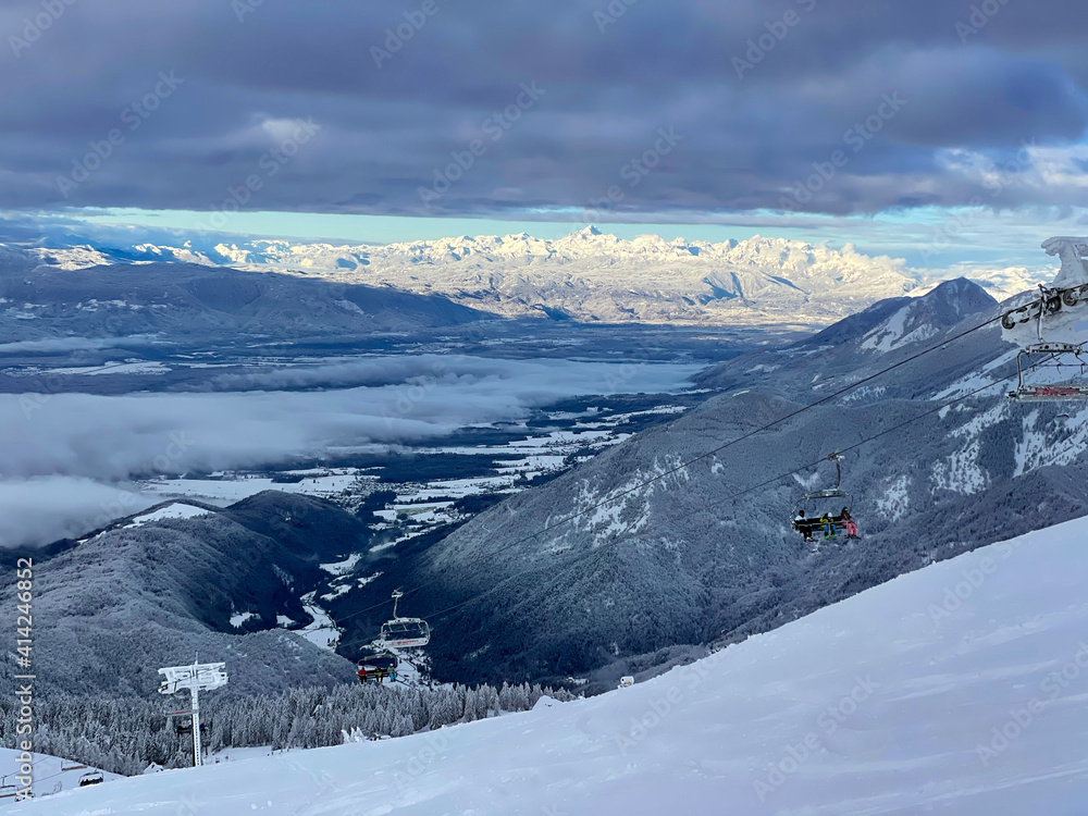一台正在运行的滑雪缆车沿着斜坡向上移动，俯瞰冬日山谷的风景。