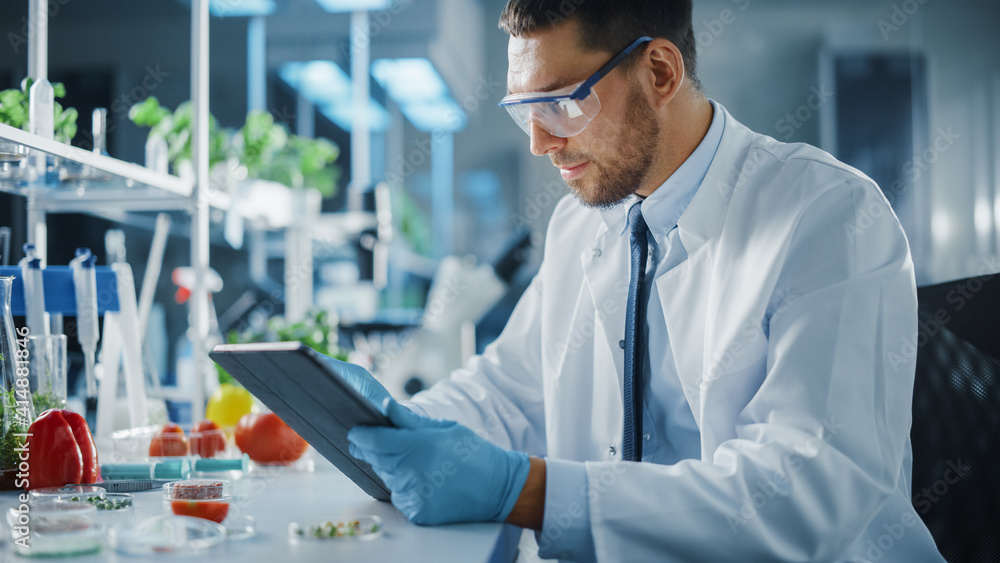 男性微生物学家在数字平板电脑上工作，并创造实验室种植的蔬菜。Microbiolo