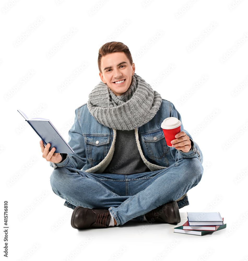 Young man with cup of coffee reading books on white background
