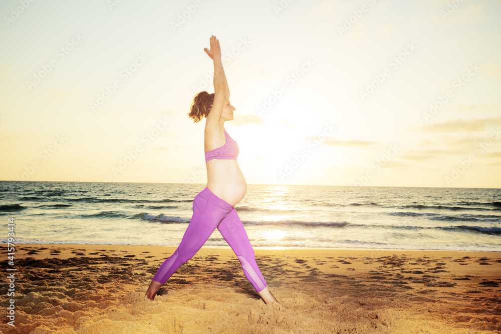 孕妇在沙滩上锻炼伸展运动，背对大海日落