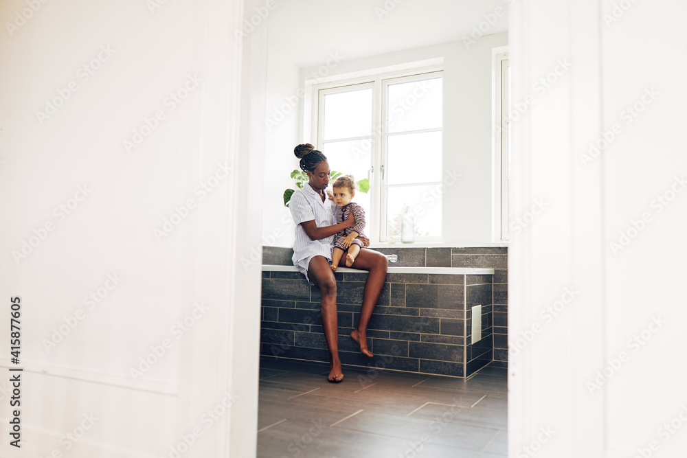 年轻的妈妈和小女孩坐在家里的浴室里