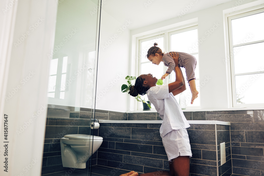 Young mom holding her little girl in their bathroom at home