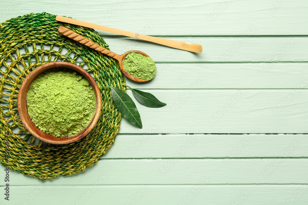 Bowl with powdered matcha tea, chashaku and spoon on color wooden background