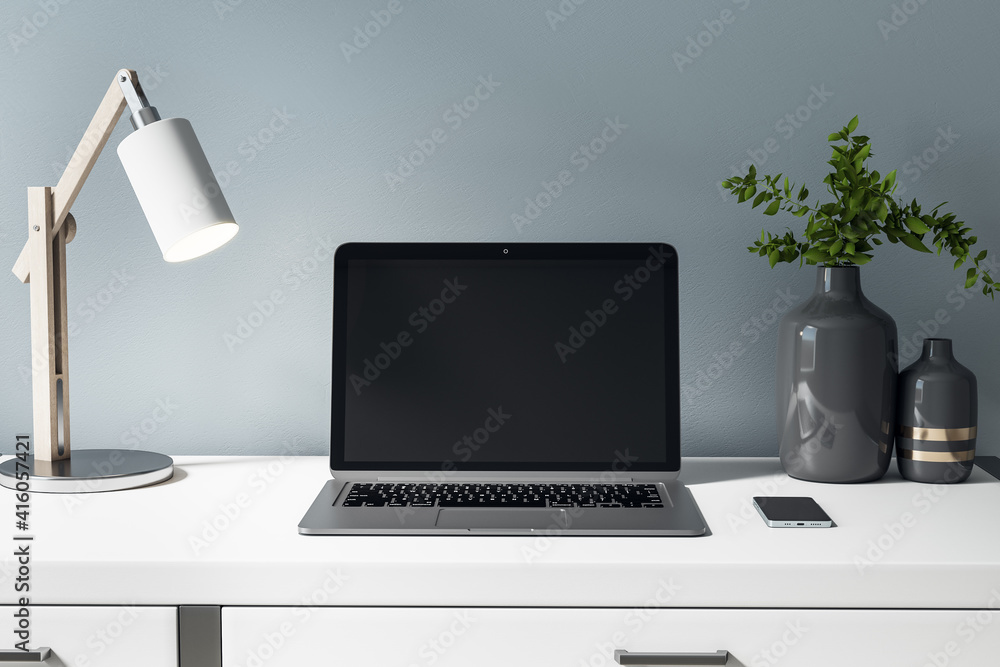 Front view on blank black laptop display on white table with stylish vase, lamp and smartphone. Mock
