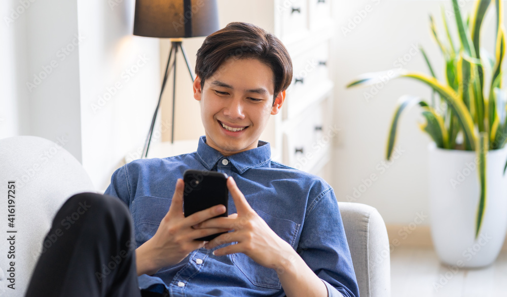 Young Asian man lying on sofa and using phone
