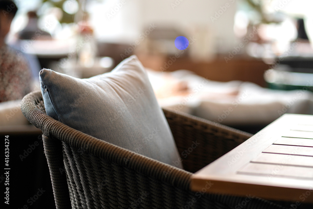 封闭式彩色软枕头，软垫布置在带有模糊庭院区域的自然材料餐椅上