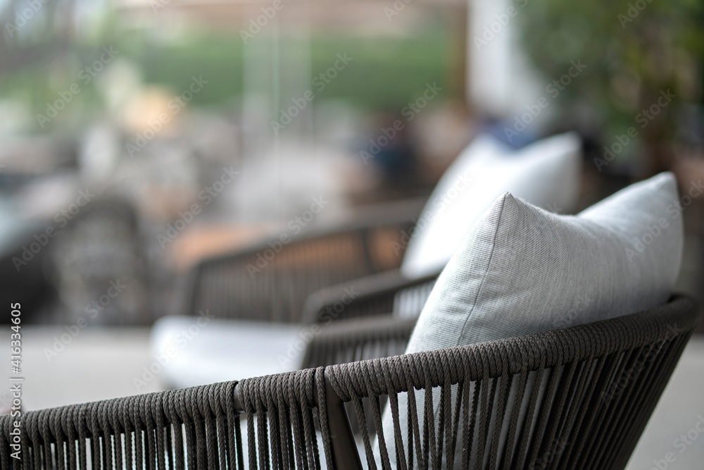 封闭式彩色软枕头，软垫布置在带有模糊庭院区域的自然材料餐椅上