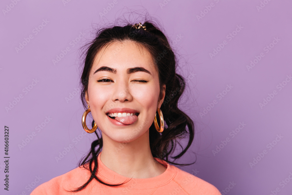 快乐的亚洲女孩做着有趣的脸。戴着耳环的时尚日本年轻女性的正面图。