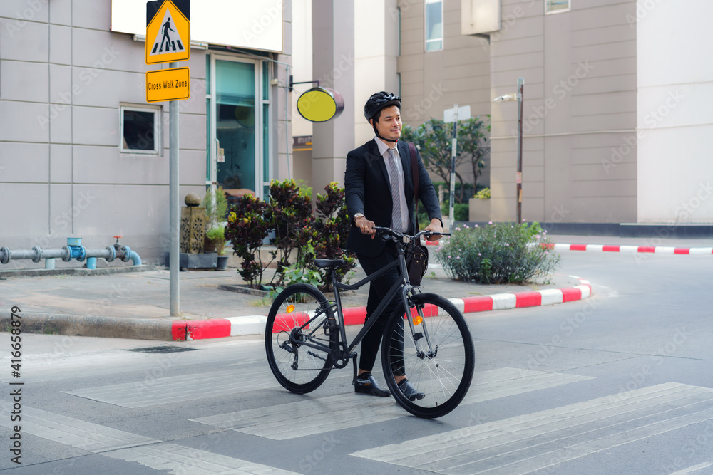 亚洲商人在早上通勤时推着自行车穿过城市街道上的人行横道。