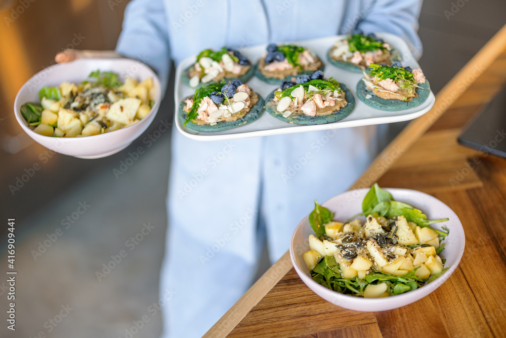 穿着蓝色衬衫的女人在盘子里放着一套开胃菜，里面有海藻、奶酪、蓝莓和鹰嘴豆泥。