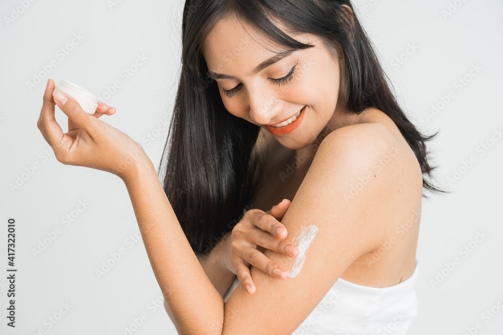 年轻的皮肤护理亚洲女性在手臂和肩膀上涂抹身体乳液