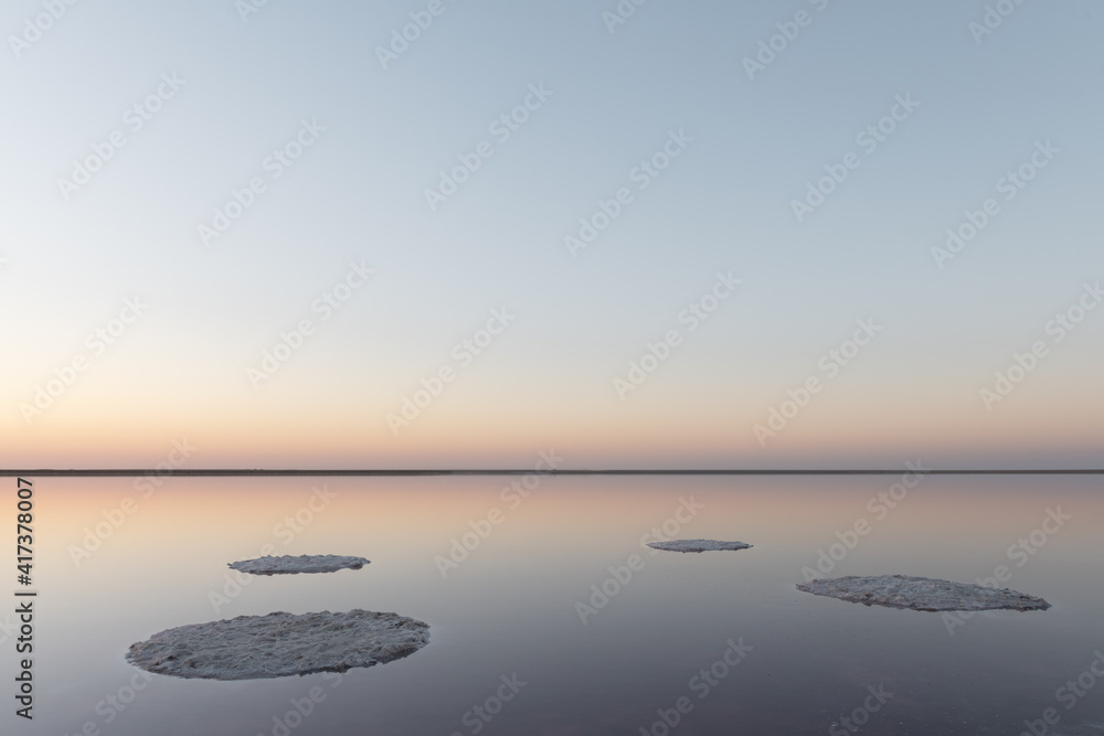 宁静的极简主义景观，粉红色的盐湖表面光滑，平静的水与地平线